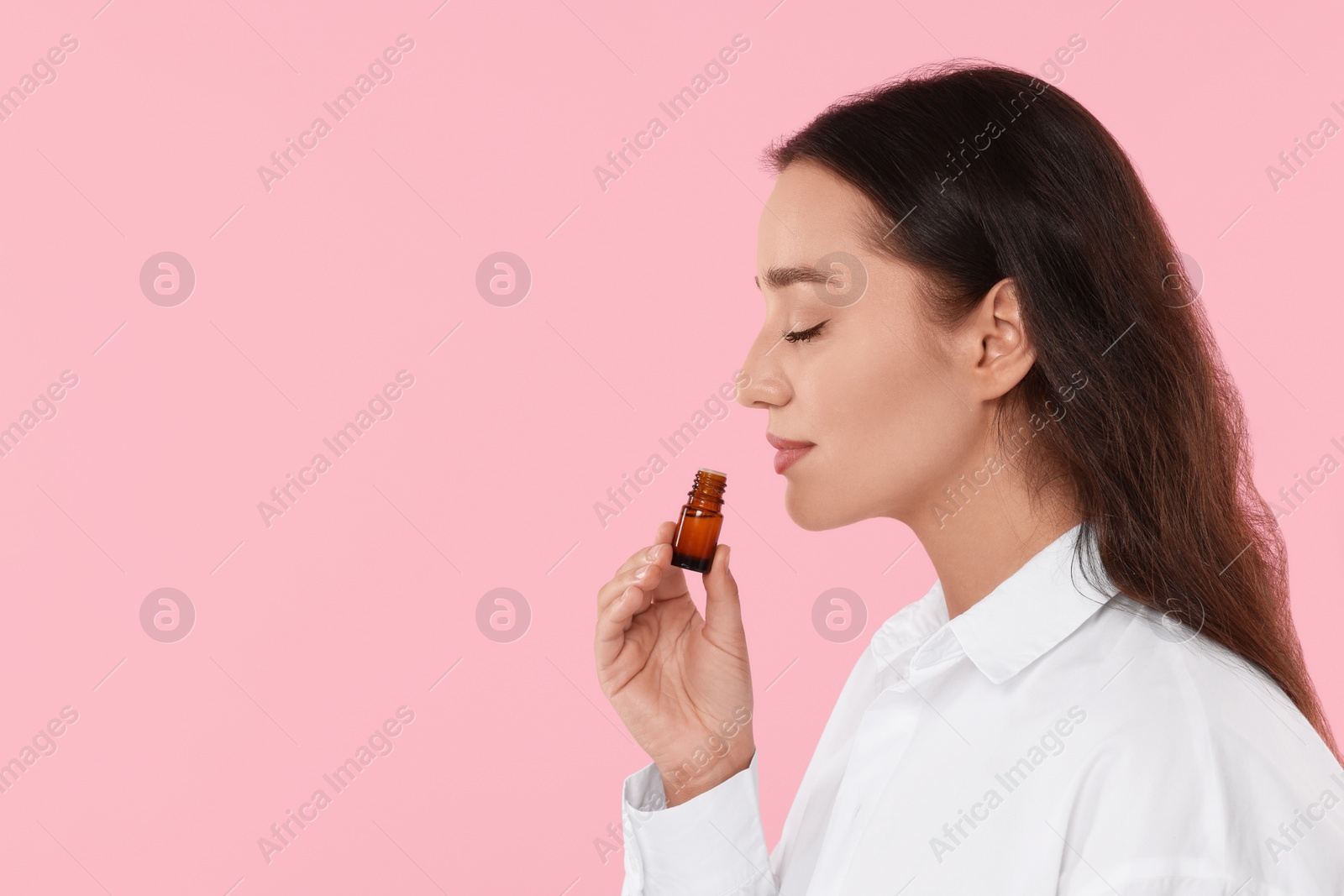 Photo of Beautiful young woman with bottle of essential oil on pink background, space for text