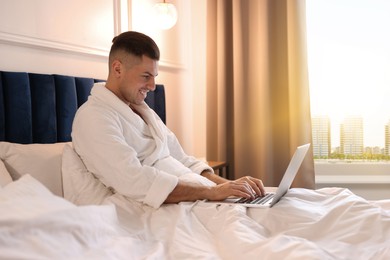 Image of Handsome man working with laptop on bed in hotel room