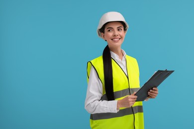 Engineer in hard hat holding clipboard on light blue background, space for text