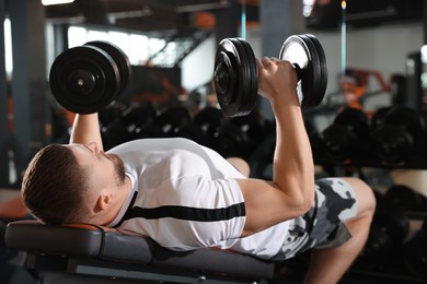 Athletic man training with dumbbells in gym