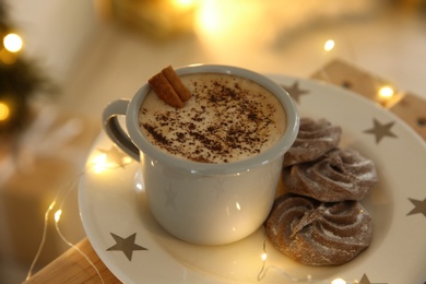 Tasty hot drink and chocolate cookies surrounded by Christmas lights, closeup