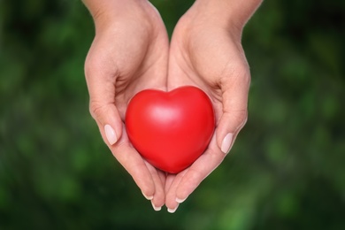 Photo of Young woman holding red heart on blurred green background, closeup. Donation concept