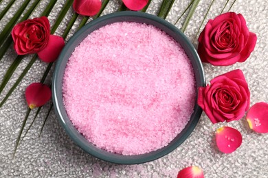 Photo of Natural sea salt in bowl, rose flowers and petals on grey textured table, flat lay