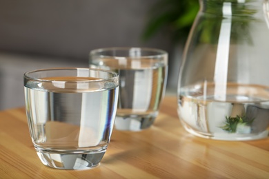 Jug and glasses of water on wooden table in room. Refreshing drink