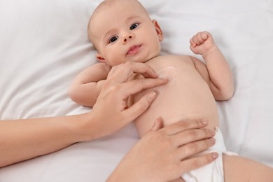 Woman applying body cream onto baby`s skin on bed, closeup