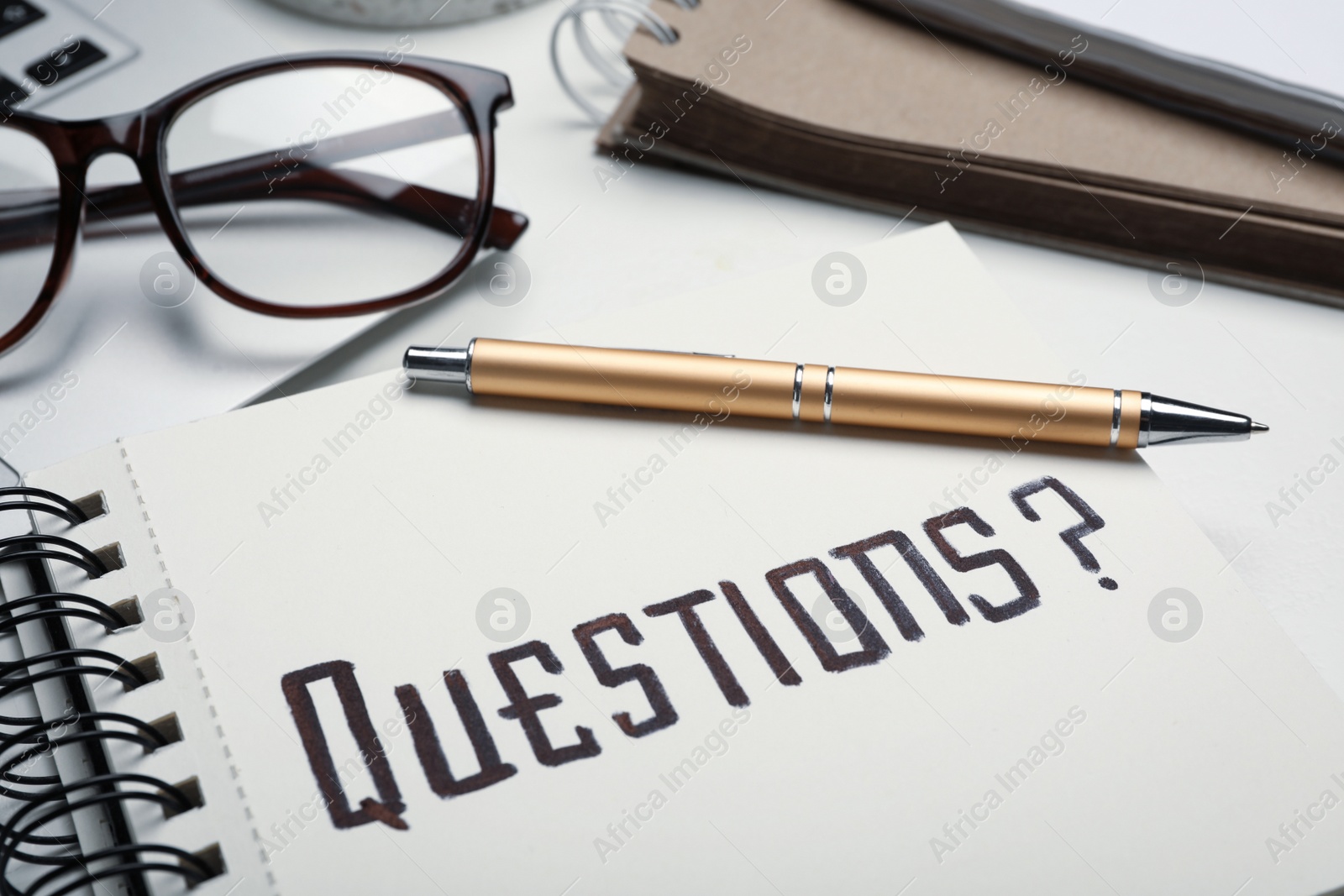 Photo of Notebook with word QUESTIONS and pen on table, closeup