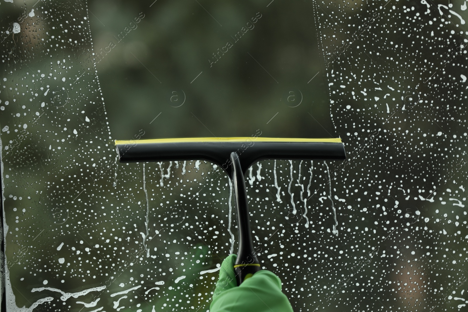 Photo of Woman cleaning glass with squeegee indoors, closeup