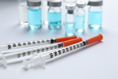 Disposable syringes with needles and vials on white background, closeup