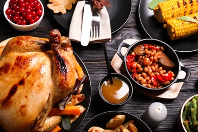Photo of Traditional Thanksgiving day feast with delicious cooked turkey and other seasonal dishes served on black wooden table, flat lay