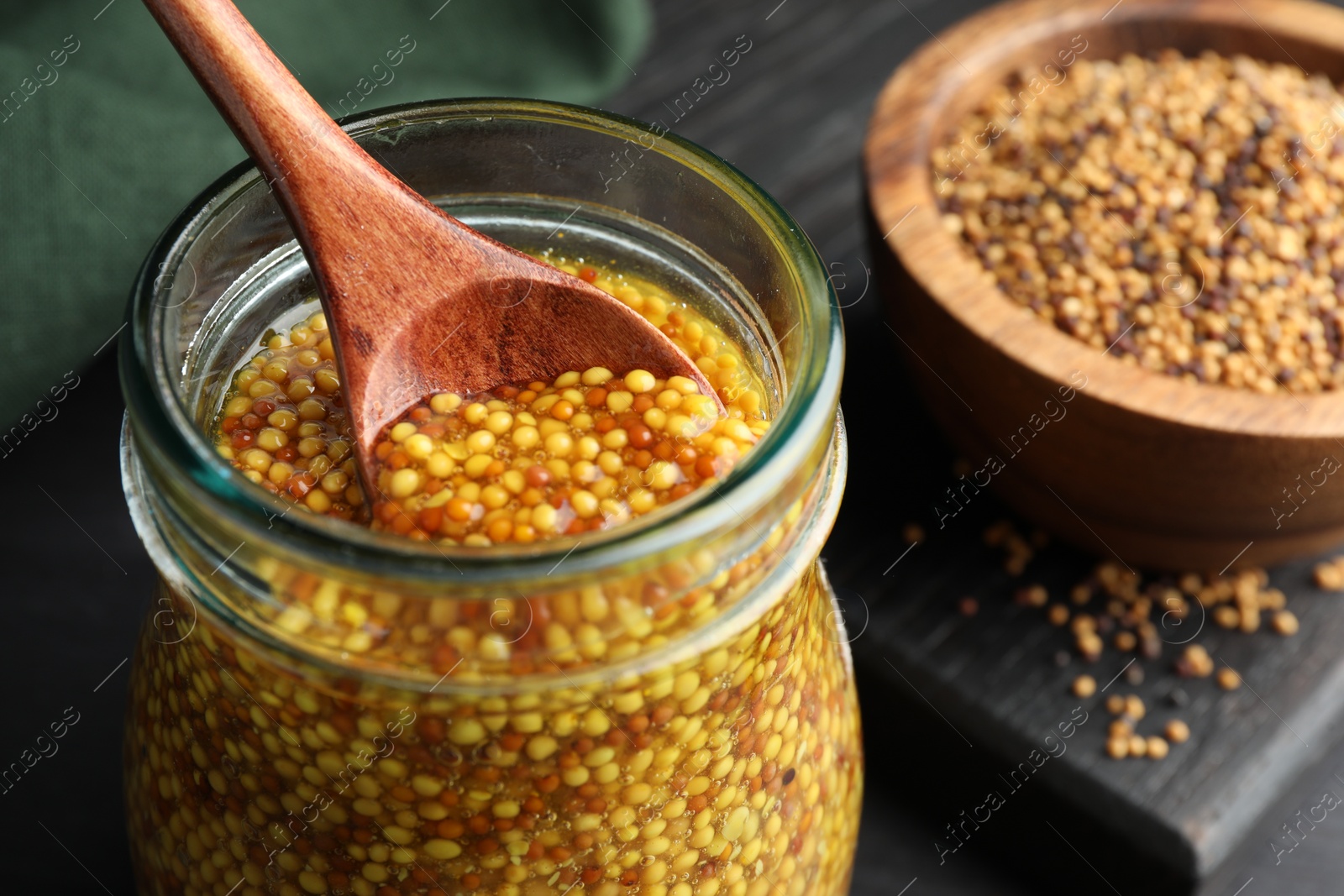 Photo of Taking whole grain mustard with spoon from jar on table, closeup