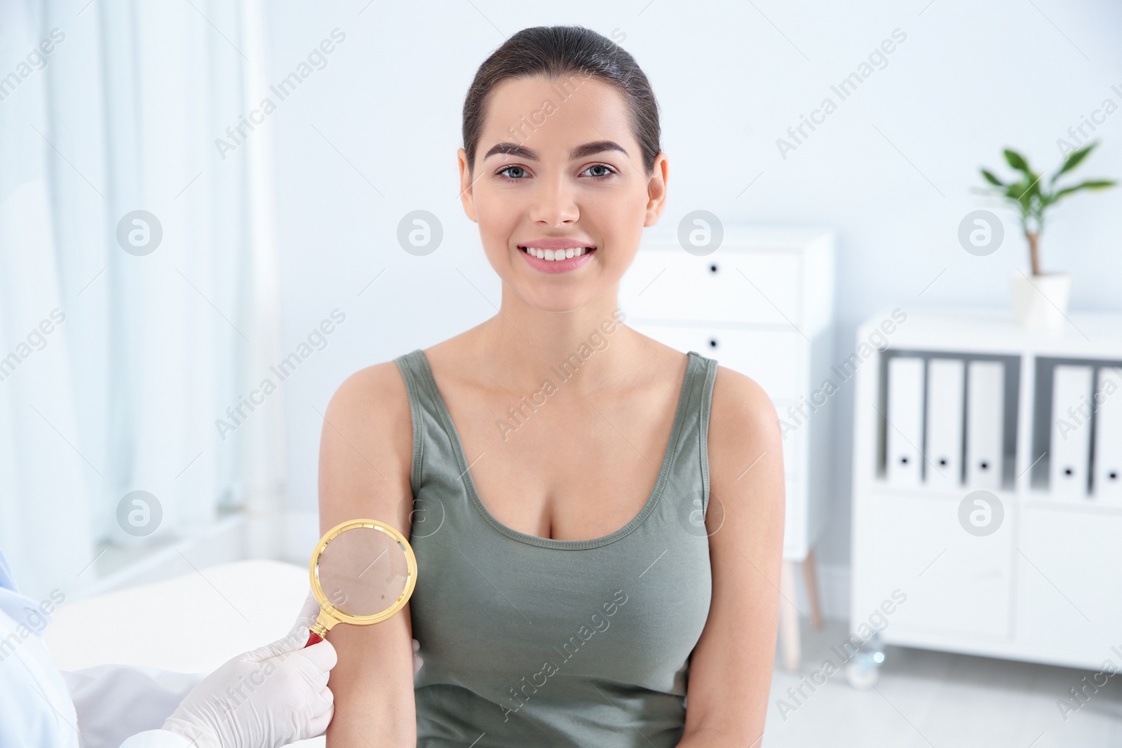 Photo of Dermatologist examining patient's birthmark with magnifying glass in clinic