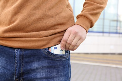 Photo of Man putting money into pocket of jeans outdoors, closeup