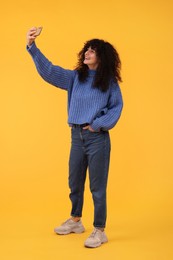 Beautiful young woman taking selfie with smartphone on orange background