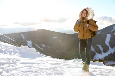 Happy young woman with backpack spending winter vacation in mountains. Space for text