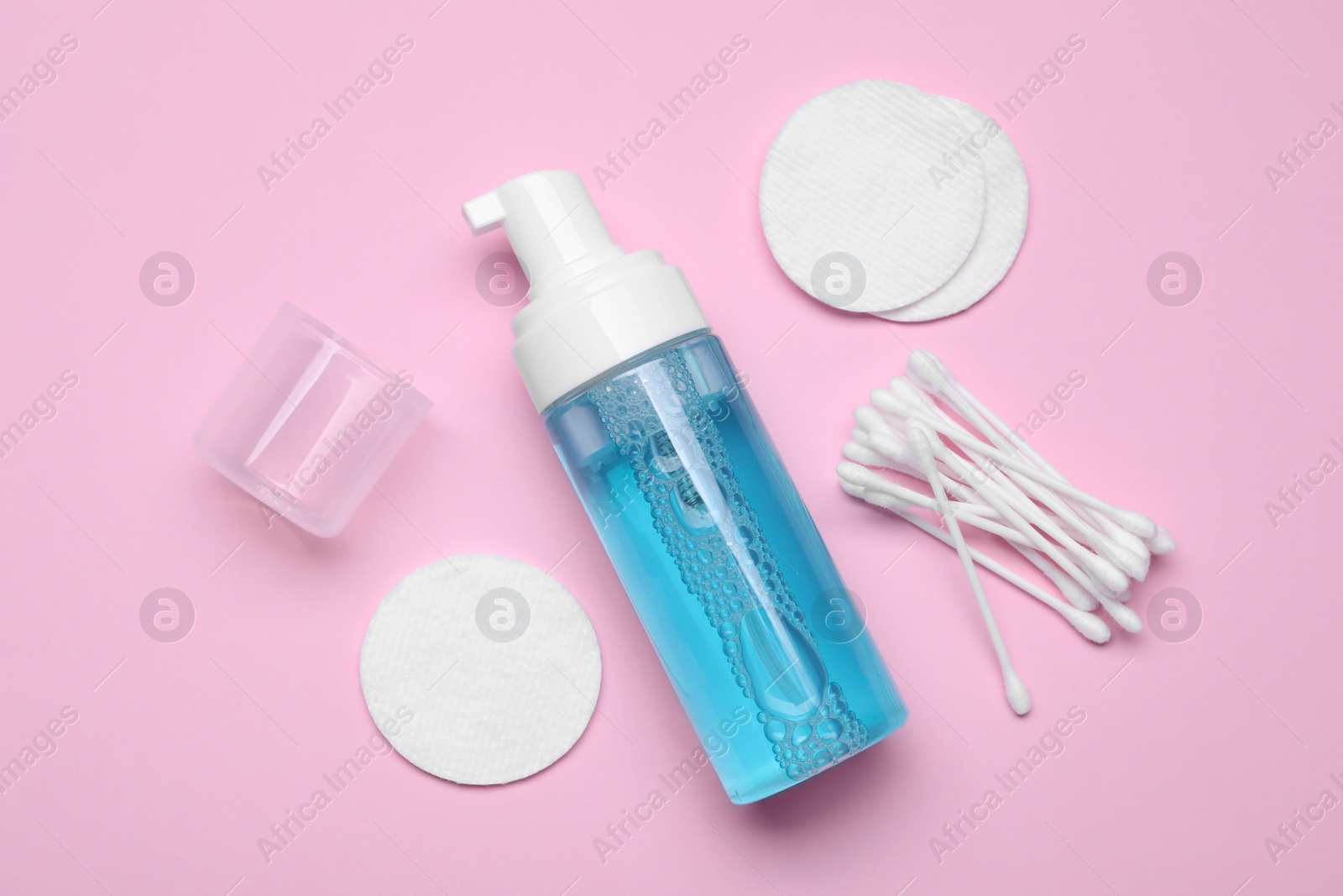 Photo of Bottle of face cleansing product, cotton buds and pads on pink background, flat lay. Space for text