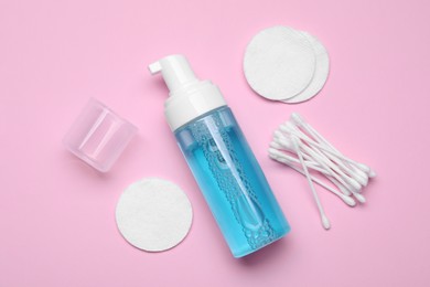 Photo of Bottle of face cleansing product, cotton buds and pads on pink background, flat lay. Space for text