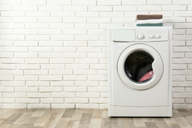 Photo of Modern washing machine with laundry and stack of towels near white brick wall. Space for text