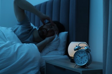 Photo of Man suffering from headache in bed at night, focus on alarm clock