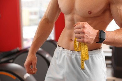 Photo of Athletic man with measuring tape in gym, closeup