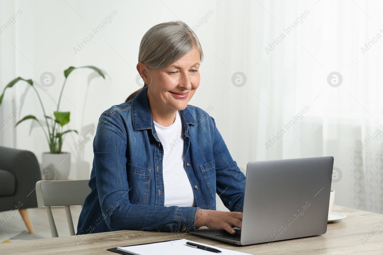 Photo of Beautiful senior woman using laptop at wooden table indoors