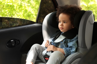 Photo of Cute African-American child sitting in safety seat inside car. Danger prevention