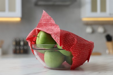 Apples in bowl covered with beeswax food wrap on white table