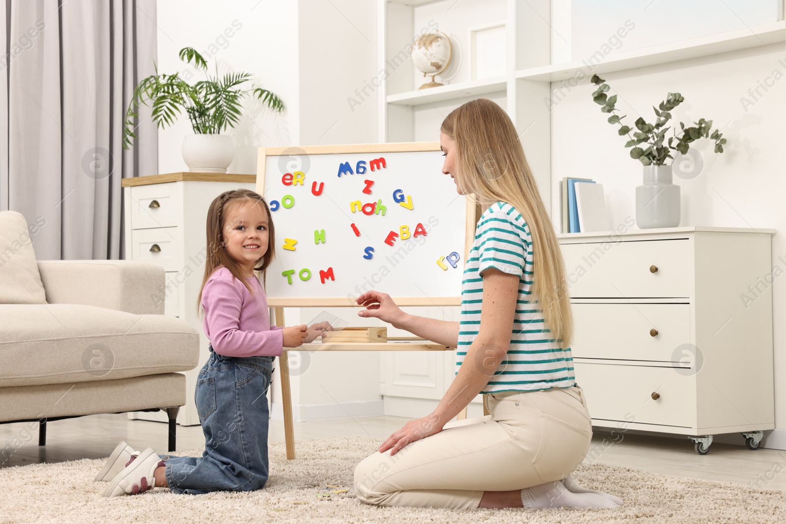 Photo of Mom teaching her daughter alphabet with magnetic letters at home