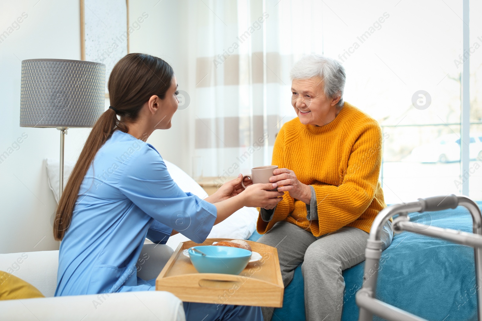 Photo of Care worker serving dinner for elderly woman in geriatric hospice