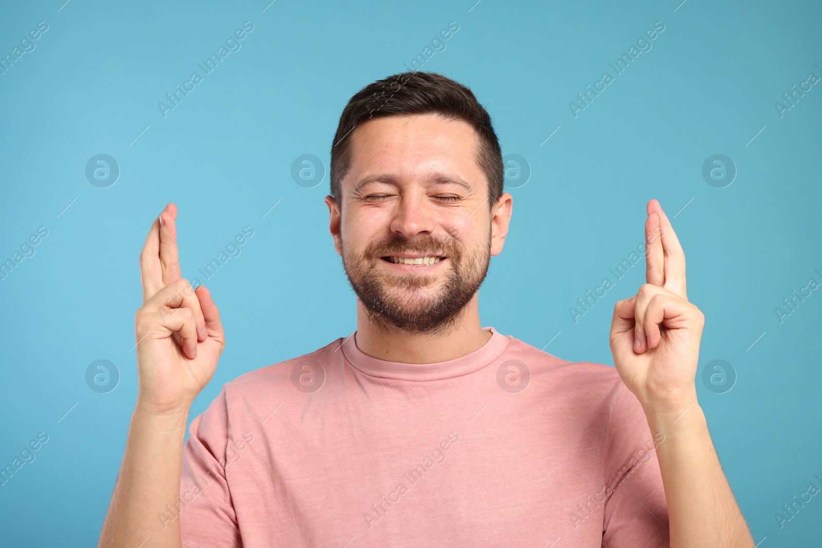 Photo of Happy man crossing his fingers on light blue background