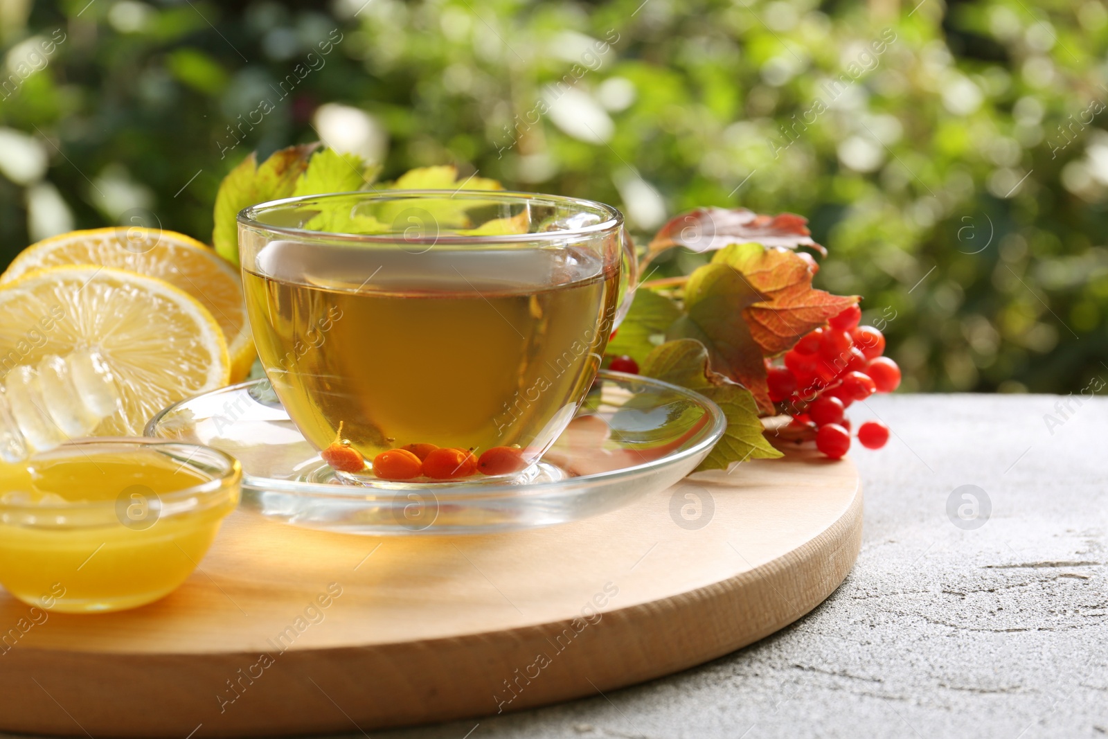 Photo of Cup of delicious tea with lemon, honey and viburnum on light grey table outdoors. Space for text