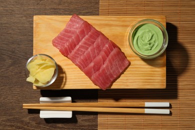 Tasty sashimi (pieces of fresh raw tuna) served with wasabi sauce and ginger slices on wooden table, top view