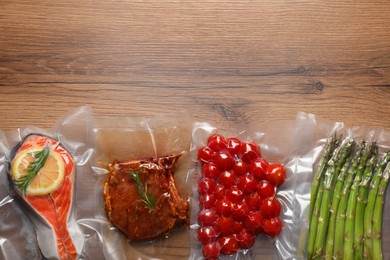 Photo of Different food products in vacuum packs on wooden table, flat lay. Space for text