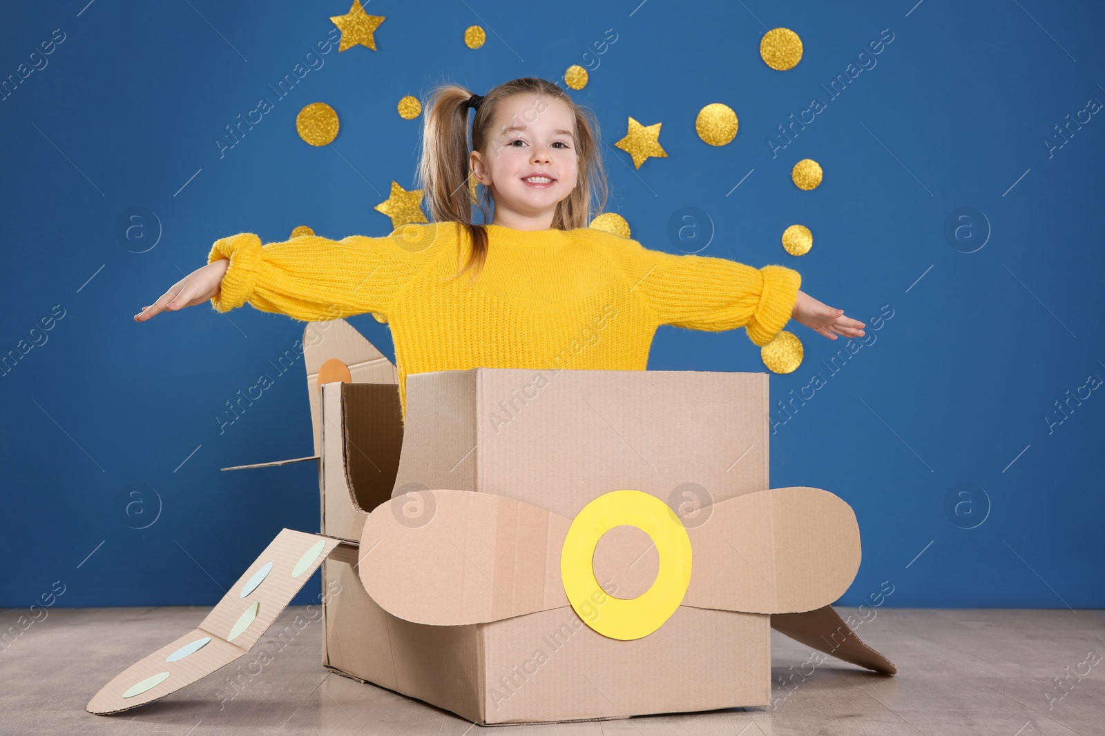 Photo of Cute little child playing with cardboard plane near blue wall