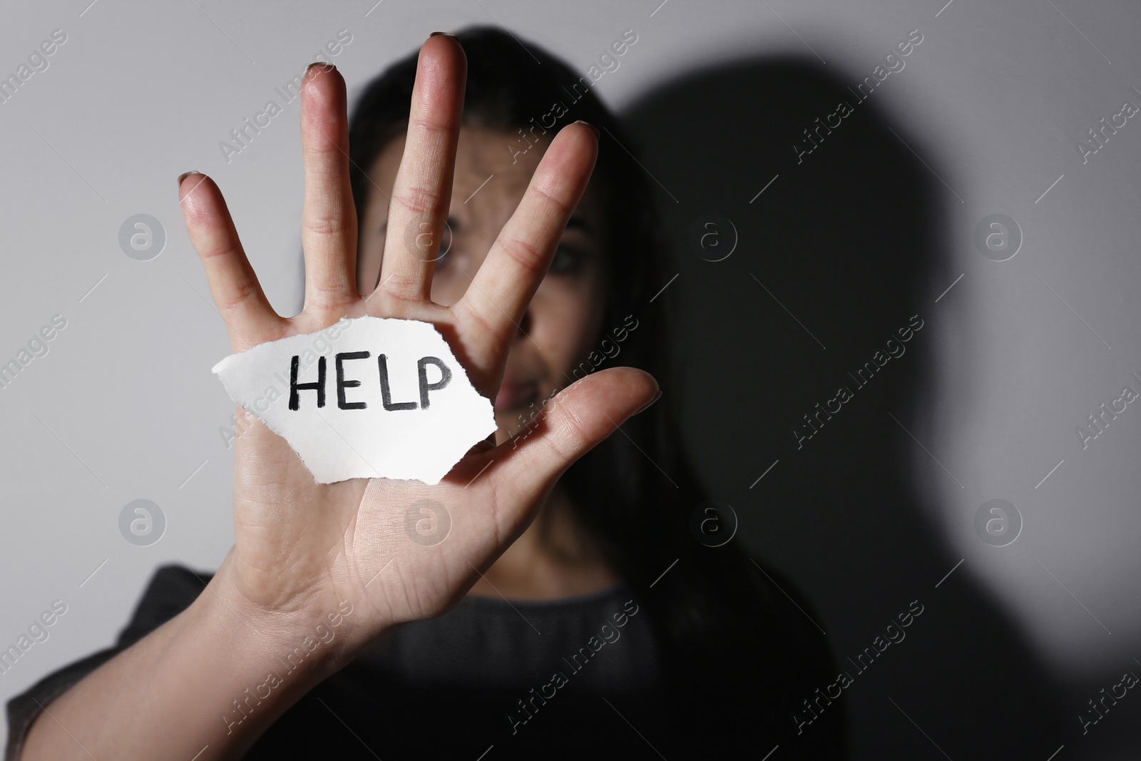 Photo of Abused young woman with sign HELP near white wall, focus on hand. Domestic violence concept