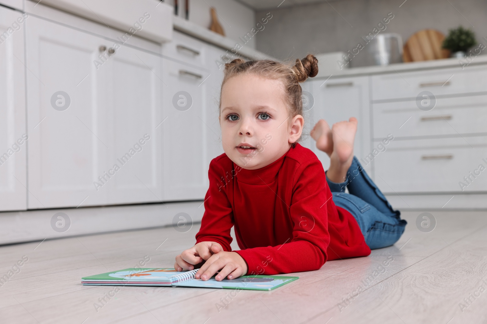 Photo of Cute little girl with book on warm floor in kitchen, space for text. Heating system