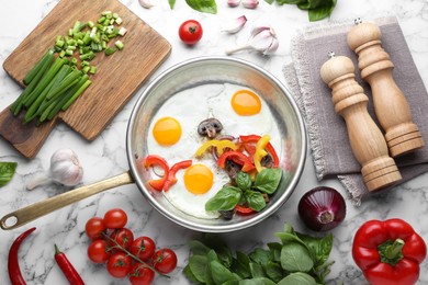Photo of Tasty fried eggs with vegetables in pan and ingredients on white marble table, flat lay