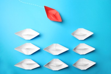 Photo of Red paper boat floating to others on light blue background, flat lay. Uniqueness concept