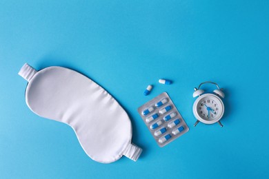 Photo of Sleeping mask, pills and alarm clock on light blue background, flat lay. Insomnia treatment