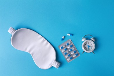 Sleeping mask, pills and alarm clock on light blue background, flat lay. Insomnia treatment