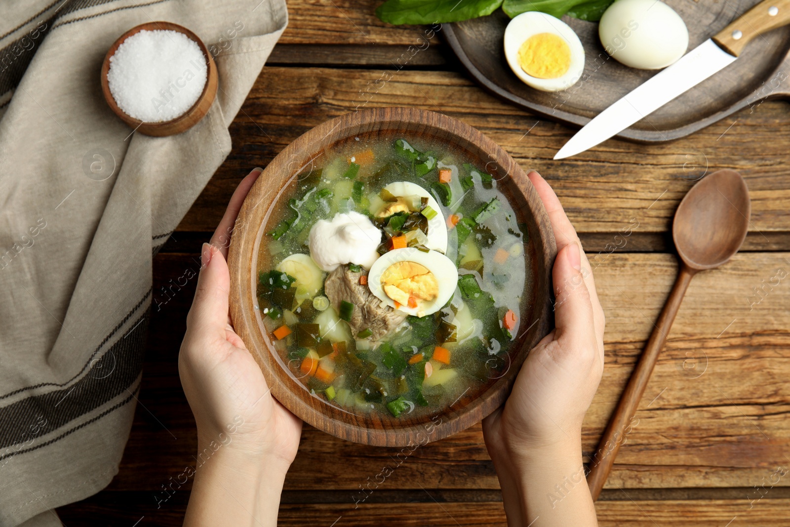 Photo of Woman eating delicious sorrel soup with meat and egg at wooden table, top view