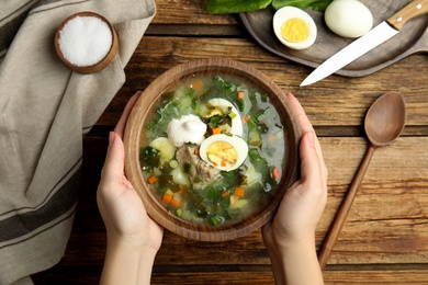 Photo of Woman eating delicious sorrel soup with meat and egg at wooden table, top view