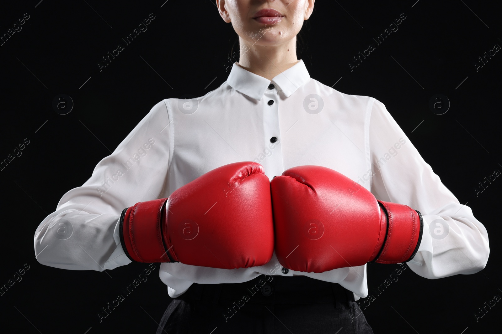 Photo of Businesswoman in shirt wearing boxing gloves on black background, closeup