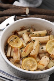 Dish with baked salsify roots, lemon and thyme on table, closeup