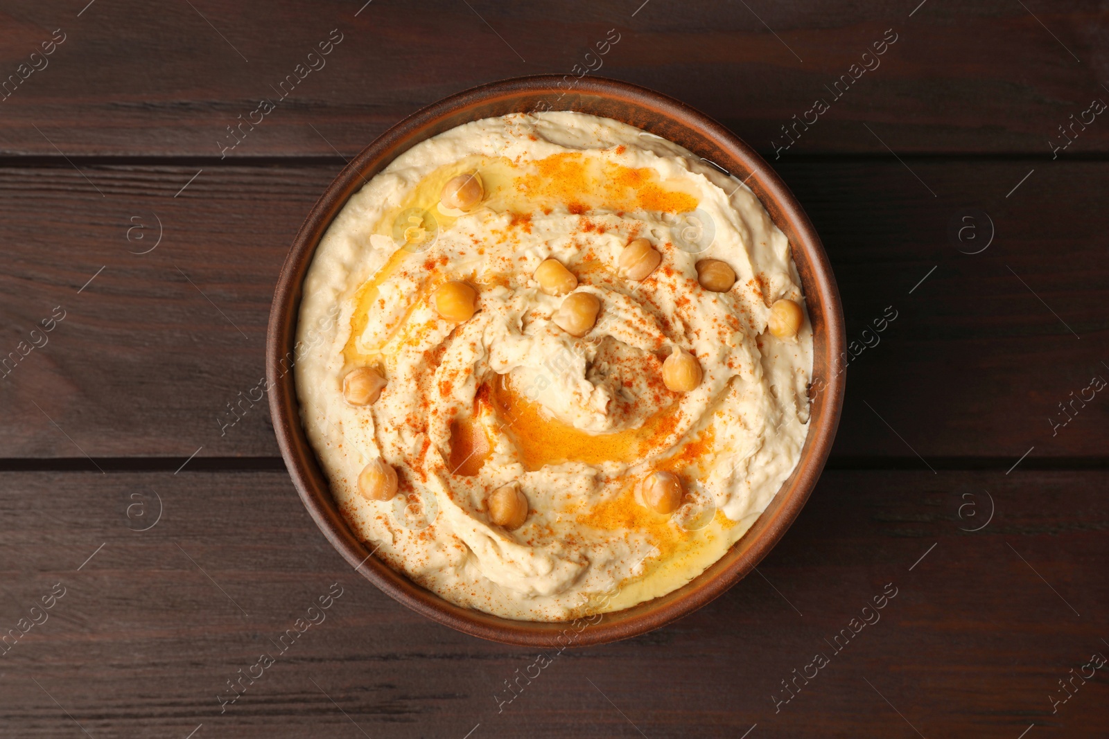 Photo of Bowl of tasty hummus with chickpeas and paprika on wooden table, top view