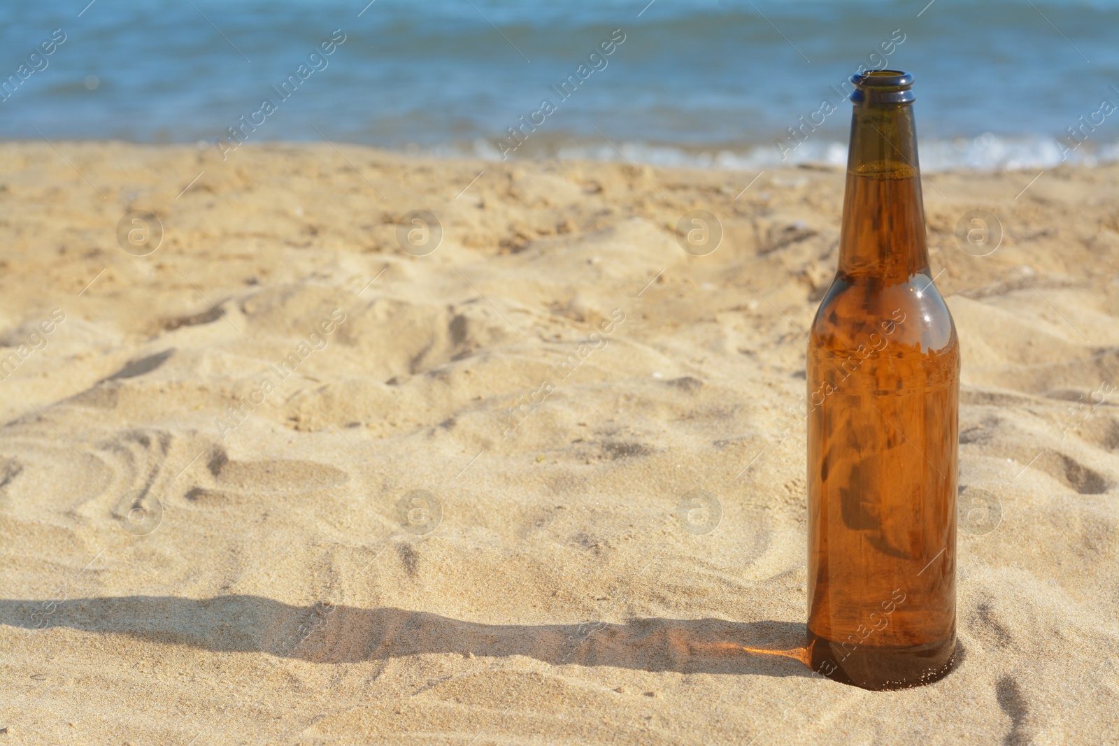Photo of Bottle of beer on sandy beach near sea. Space for text
