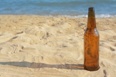 Photo of Bottle of beer on sandy beach near sea. Space for text