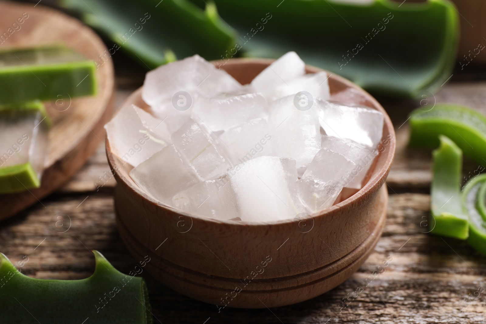 Photo of Aloe vera gel and slices of plant on wooden table, closeup