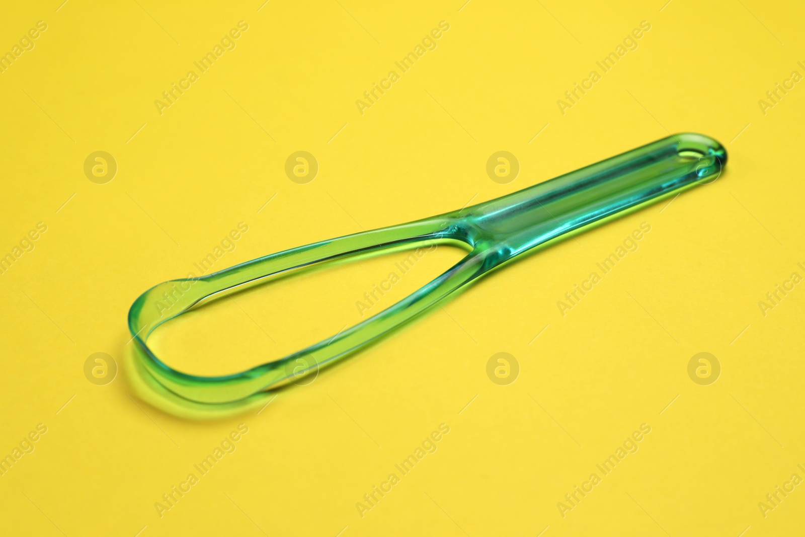 Photo of One green tongue cleaner on yellow background