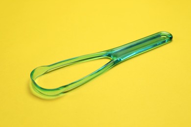 Photo of One green tongue cleaner on yellow background