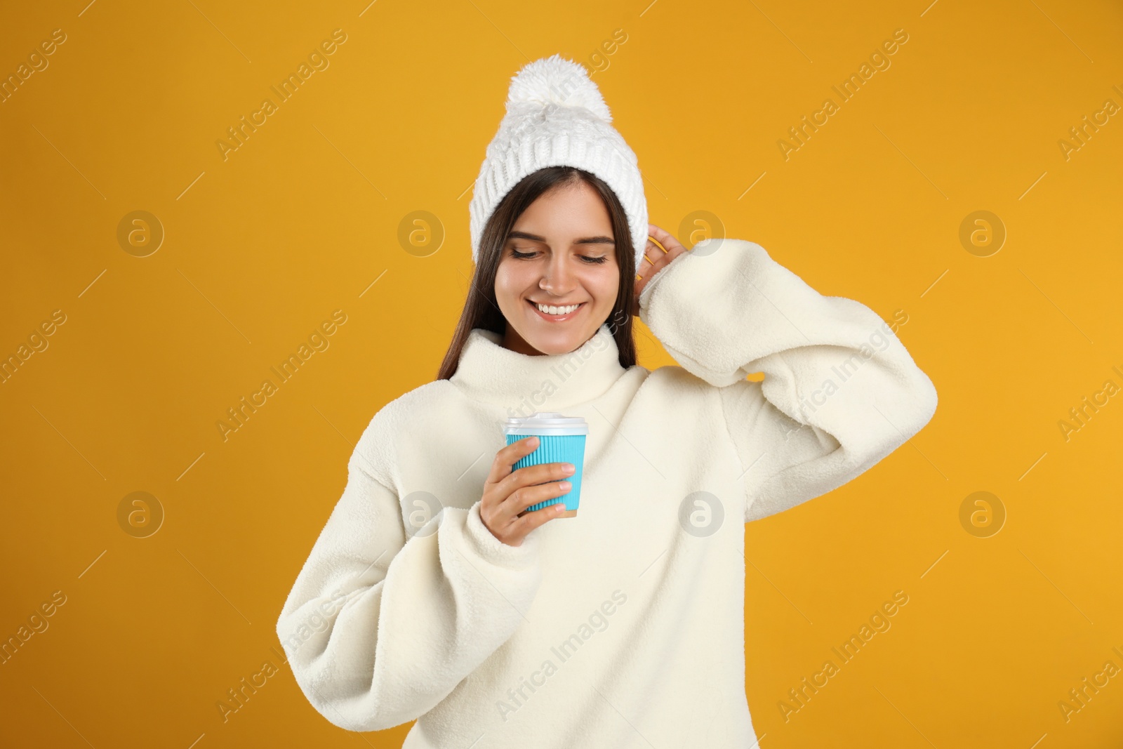 Photo of Happy beautiful woman with paper cup of mulled wine on yellow background